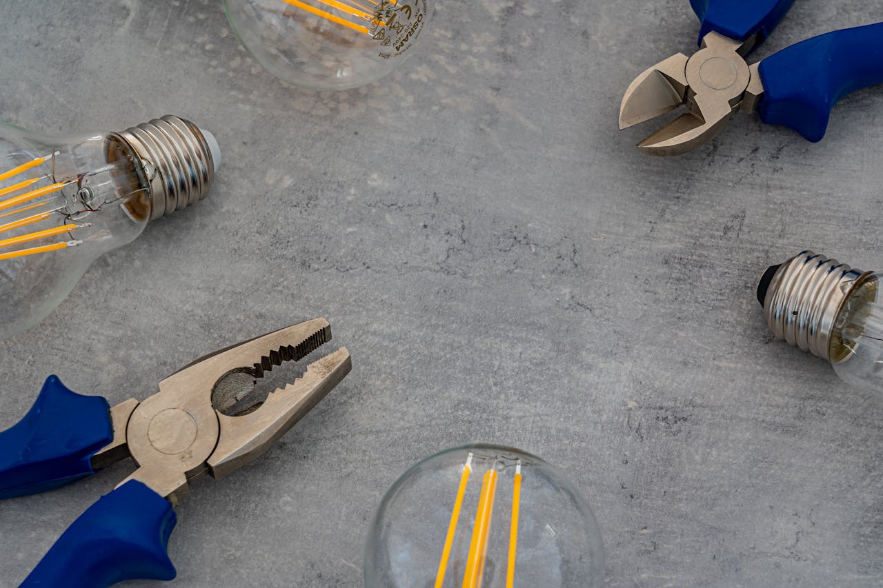 Top view of Edison bulbs and blue-handled pliers arranged on a gray concrete surface.